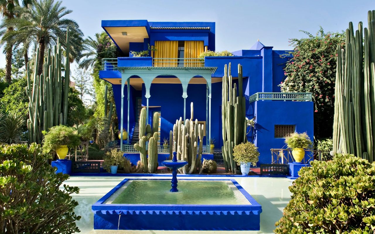 A blue-tinted Moroccan residence surrounded by tropical vegetation and fountains.