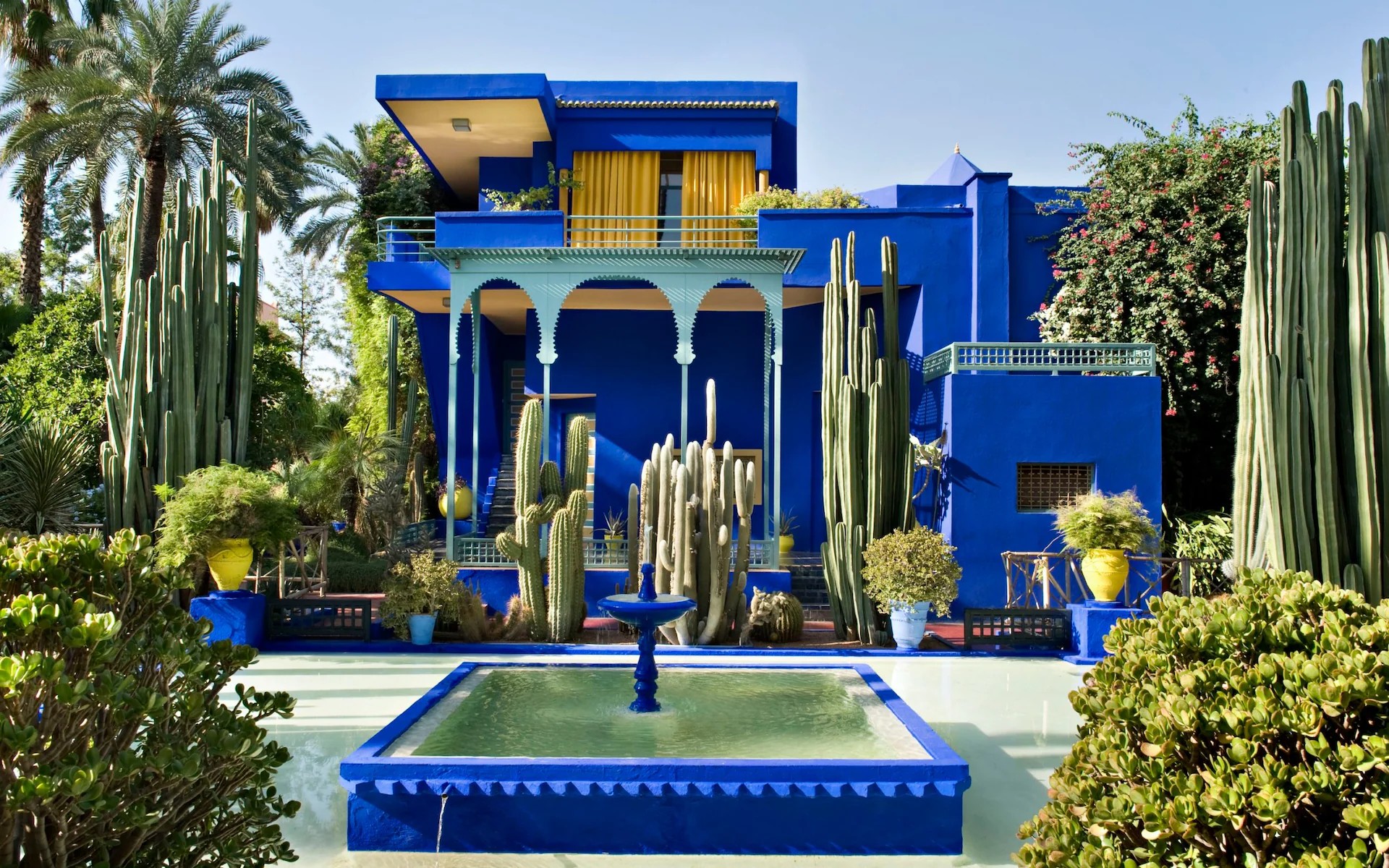 A blue-tinted Moroccan residence surrounded by tropical vegetation and fountains.