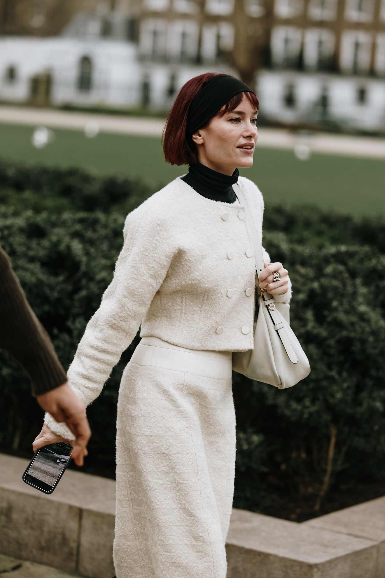 a woman wearing a white double-breasted sweate, black cardigan, and white knit skirt