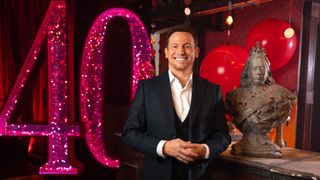 Joe Swash standing in front of a sparkly pink 40 and next to the Queen Victoria bust for EastEnders Revealed: The Lock-in