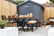 outdoor dining area with a large dining table and a black shed in a modern garden 