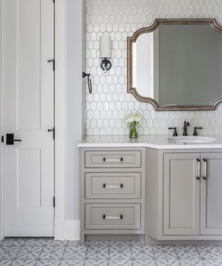 Gray bathroom with patterned floor tiles, pale gray wall, gray cabinetry, pearlescent wall tiles, mirror