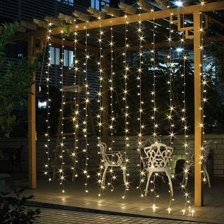 an outdoor curtain of fairy lights, next to a white outdoor dining set