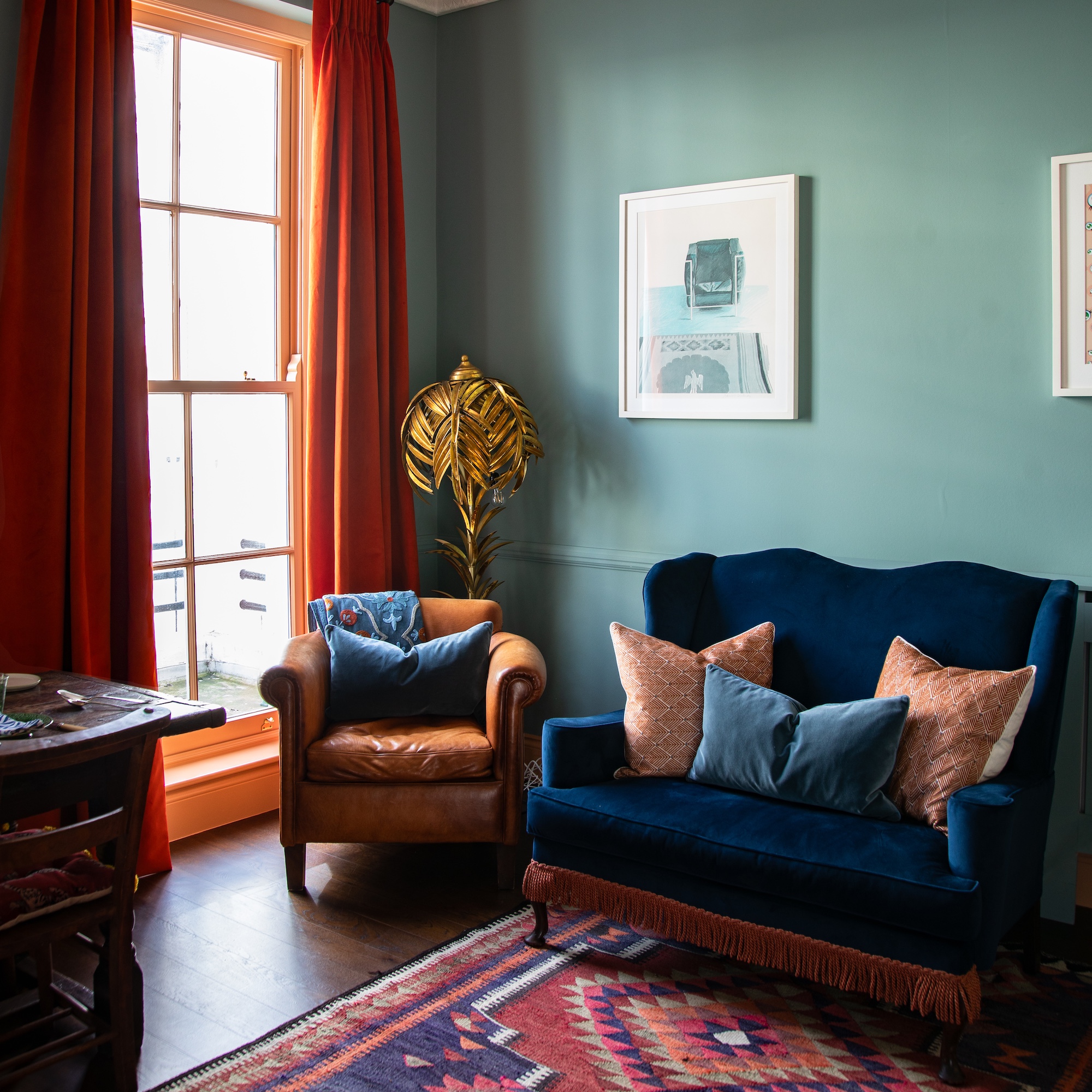 sitting room with antique blue velvet sofa, leather armchair and patterned kilim rug on floor