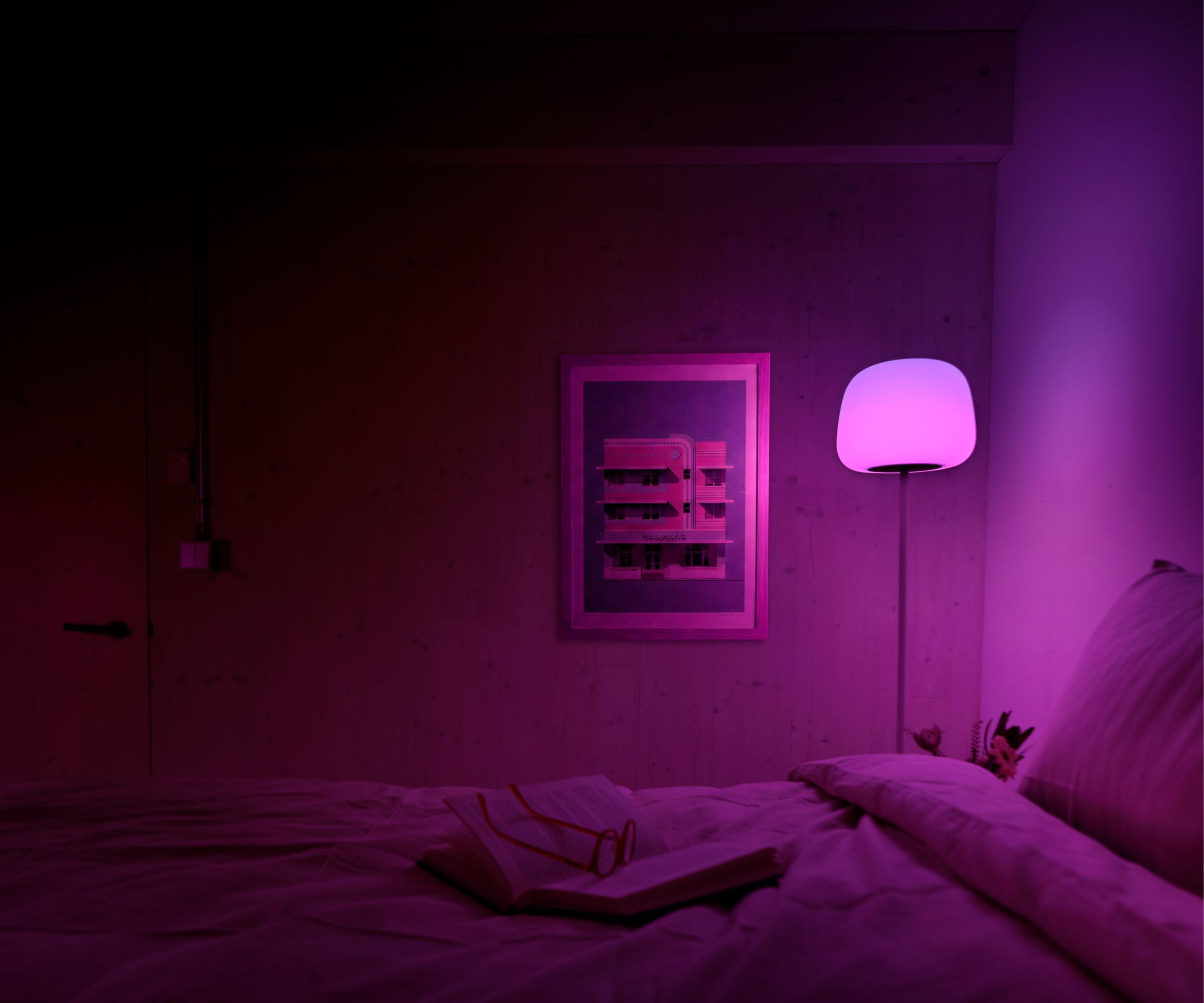 Bedroom with purple lighting from the Govee smart floor lamp, a bed and a print framed and hung on the wall