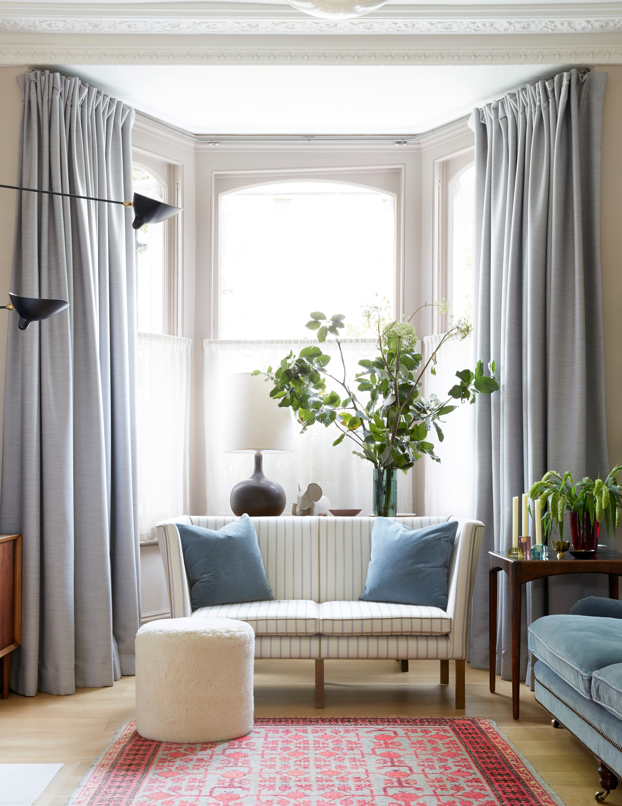 Living room with cream walls, pale blue curtains and blue sofa, striped cream sofa and red and blue rug