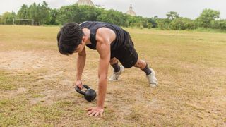 Man on grass in a plank position moving a kettlebell from one side to another