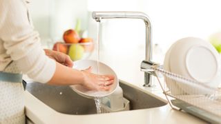 Dishes being washed by hand in the sink under running water