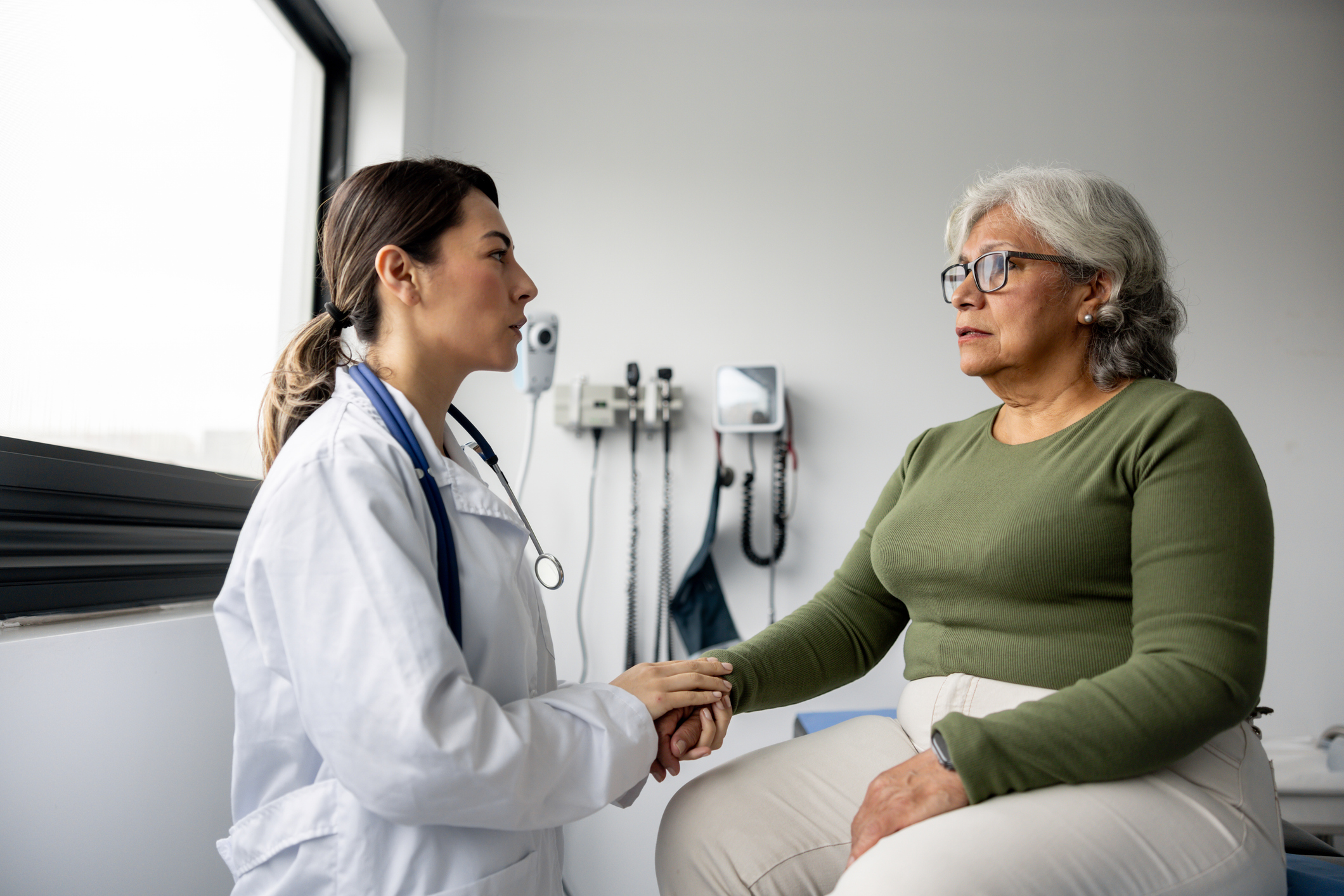 Latin American doctor consoling a senior woman and holding her hand in the consultation room &amp;ndash; healthcare and medicine concepts