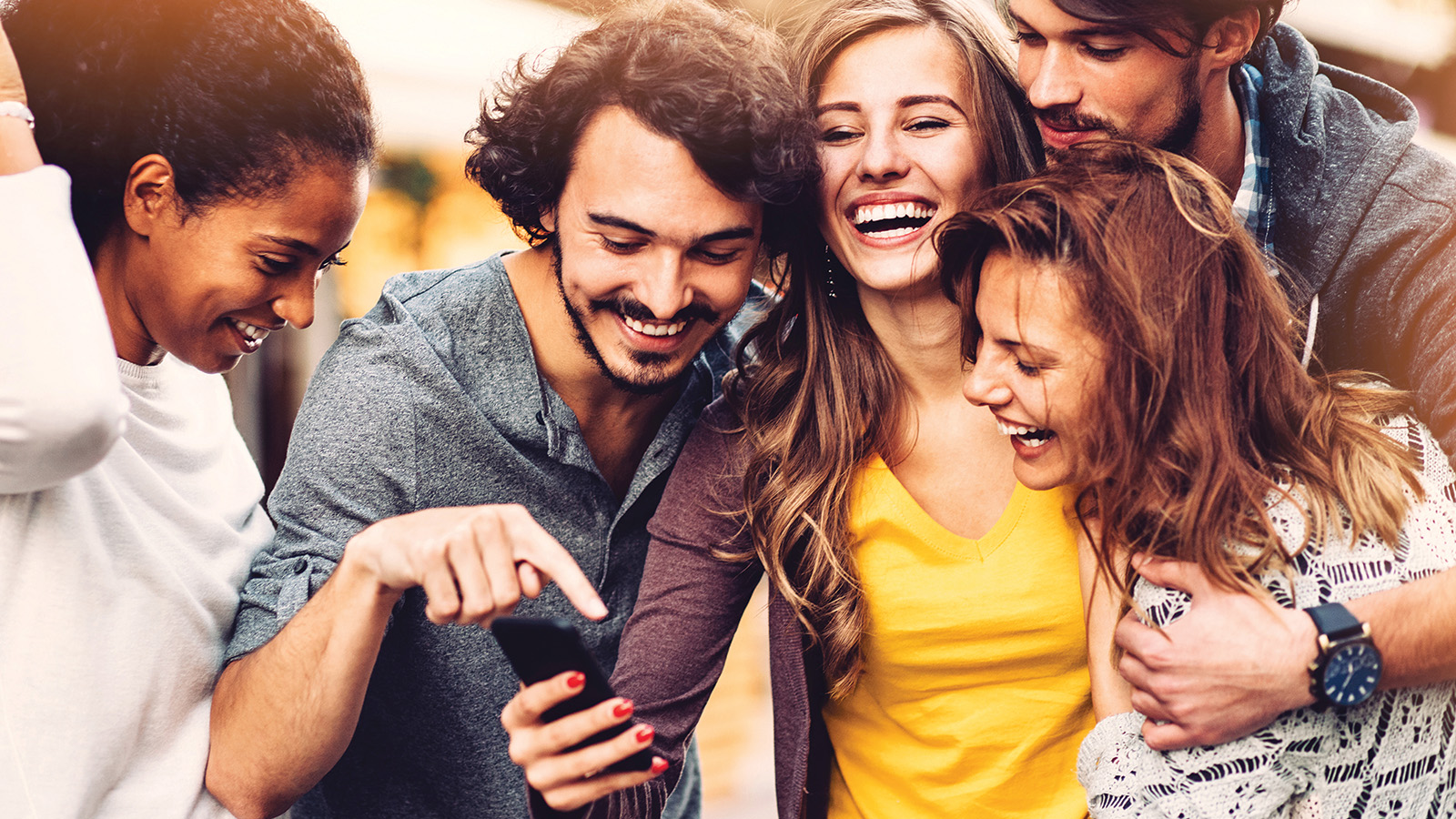 Group of young people looking at a phone, laughing