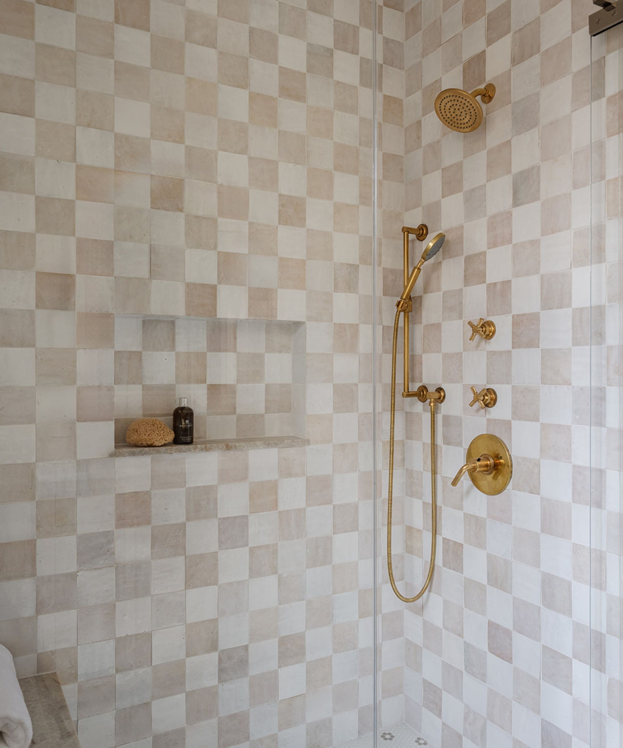 Walk in shower with gold hardware and checkerboard cream and pink tiles