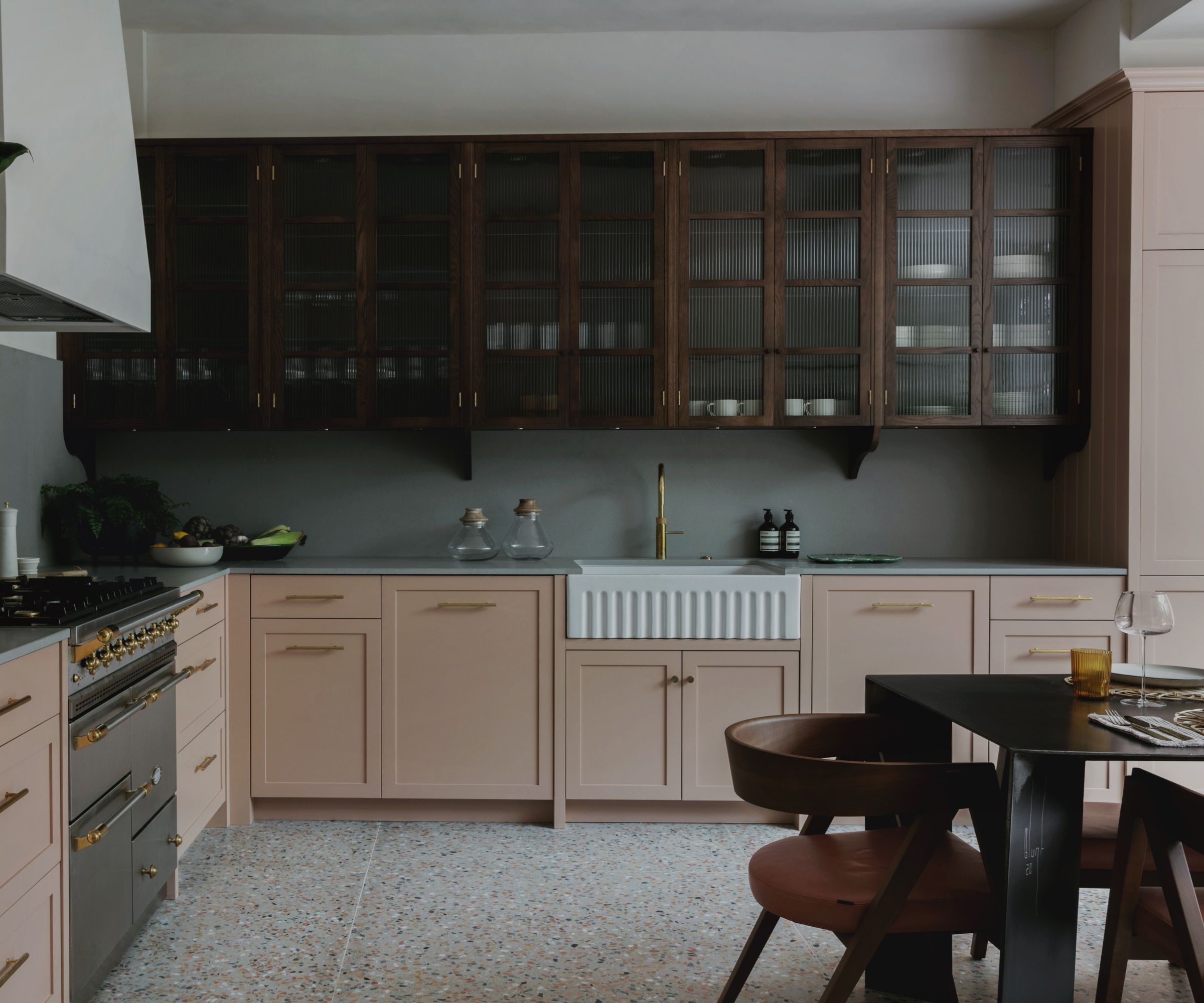 An L-shaped kitchen with pink base cabinets and glass fronted wooden upper cabinets