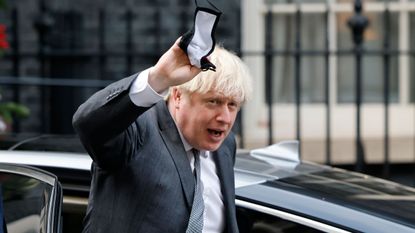 Boris Johnson gestures to members of the media as he arrives back at 10 Downing Street
