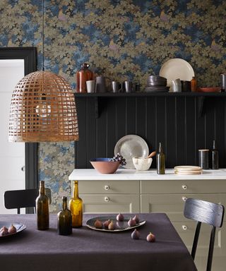 A fall color scheme in a kitchen with blue and brown leaf wallpaper, aubergine purple tablecloth, green cabinets and black backsplash