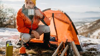 Man beside a pop-up tent in winter with hot drink