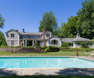 Marilyn Monroe’s house - Exterior of a french country ranch home with a grey exterior, viewed over a large outdoor pool