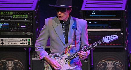 Suited and booted, wearing wraparound shades and a wide-brimmed hat, Steve Vai performs with King Crimson supergroup BEAT, playing his signature Ibanez PIA.