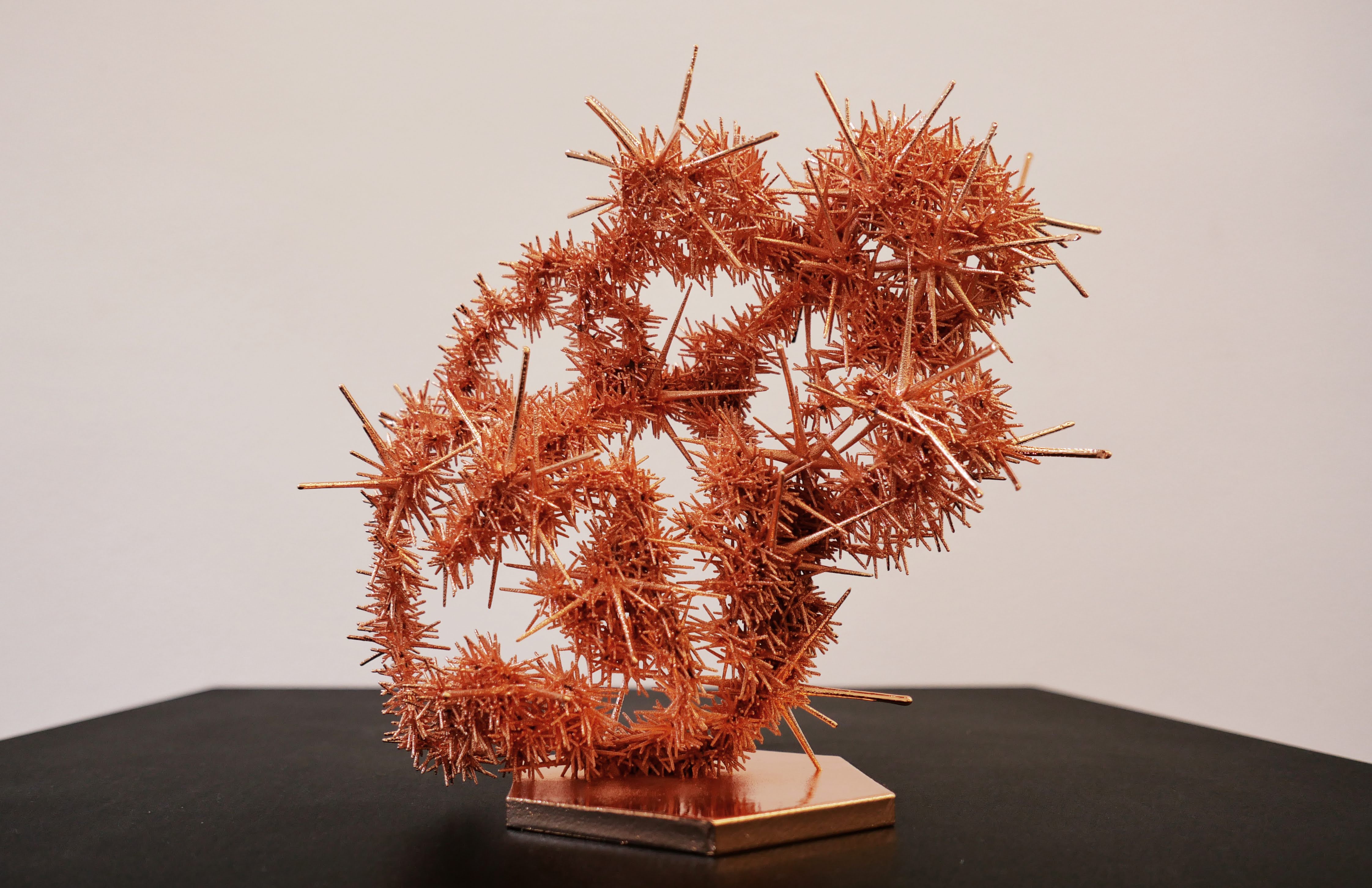 A spiky golden metal sculpture shaped like a paw with interconnected pieces sitting on a dark surface