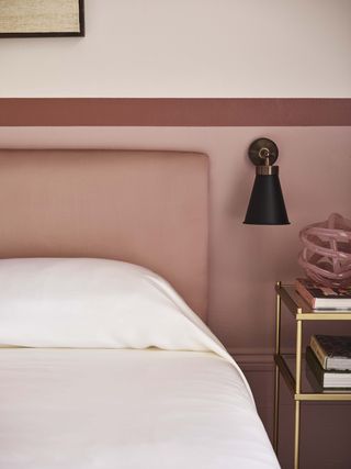 A bedroom with pink walls and white sheets styled on a bed