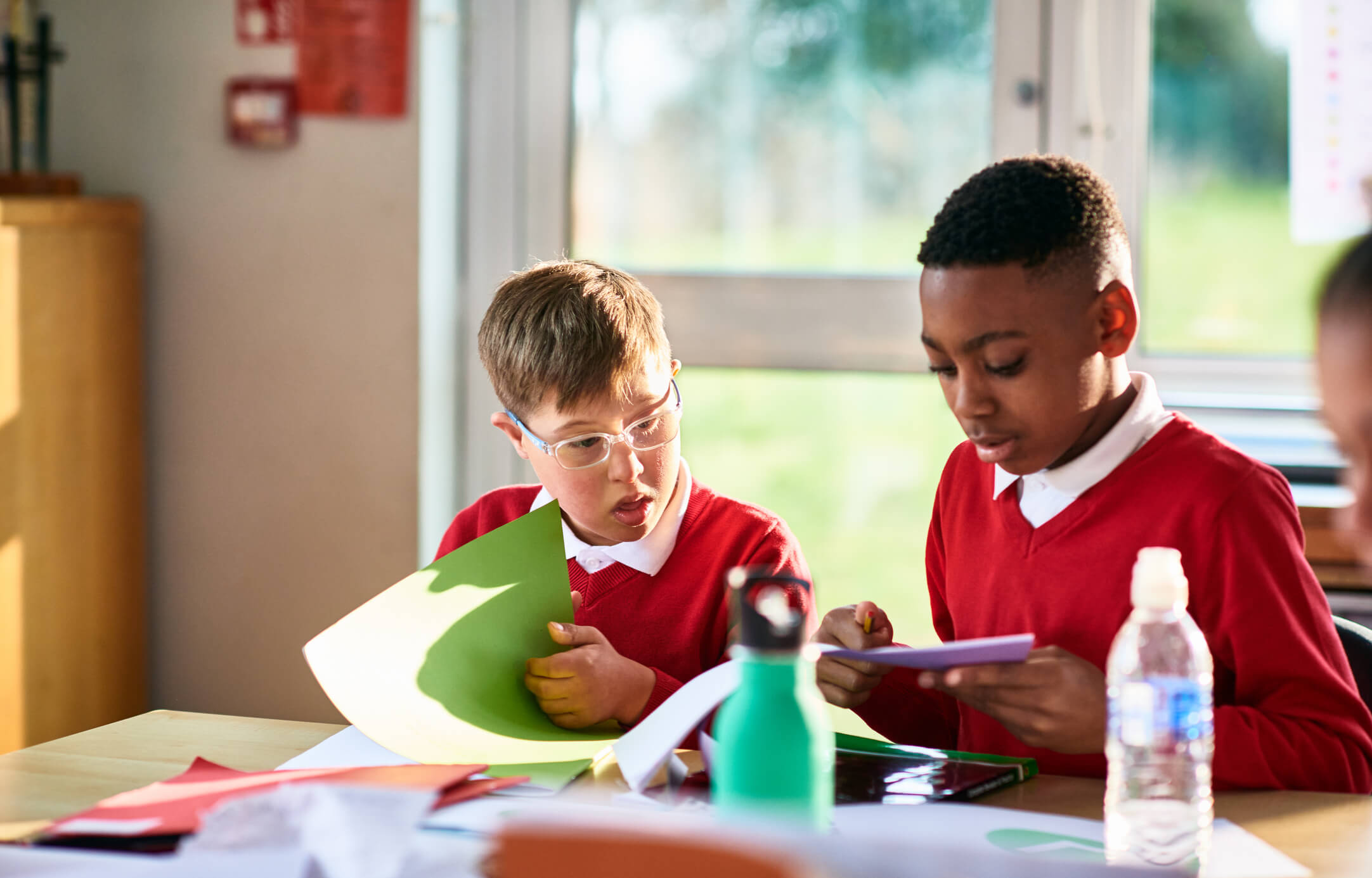 Boy with Down syndrome sitting next to another boy in classroom with books