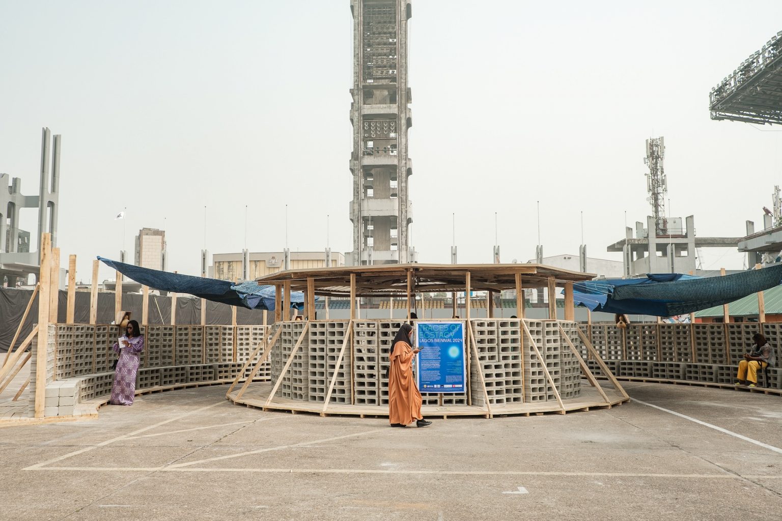 A large-scale installation features a concentric structure made of perforated bricks and wood.
