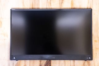 A black ASUS ZenScreen GO MB16AWP portable monitor sitting on a light wooden desk