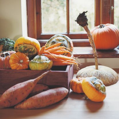 A box of autumnal produce including pumpkins and sweet potatoes