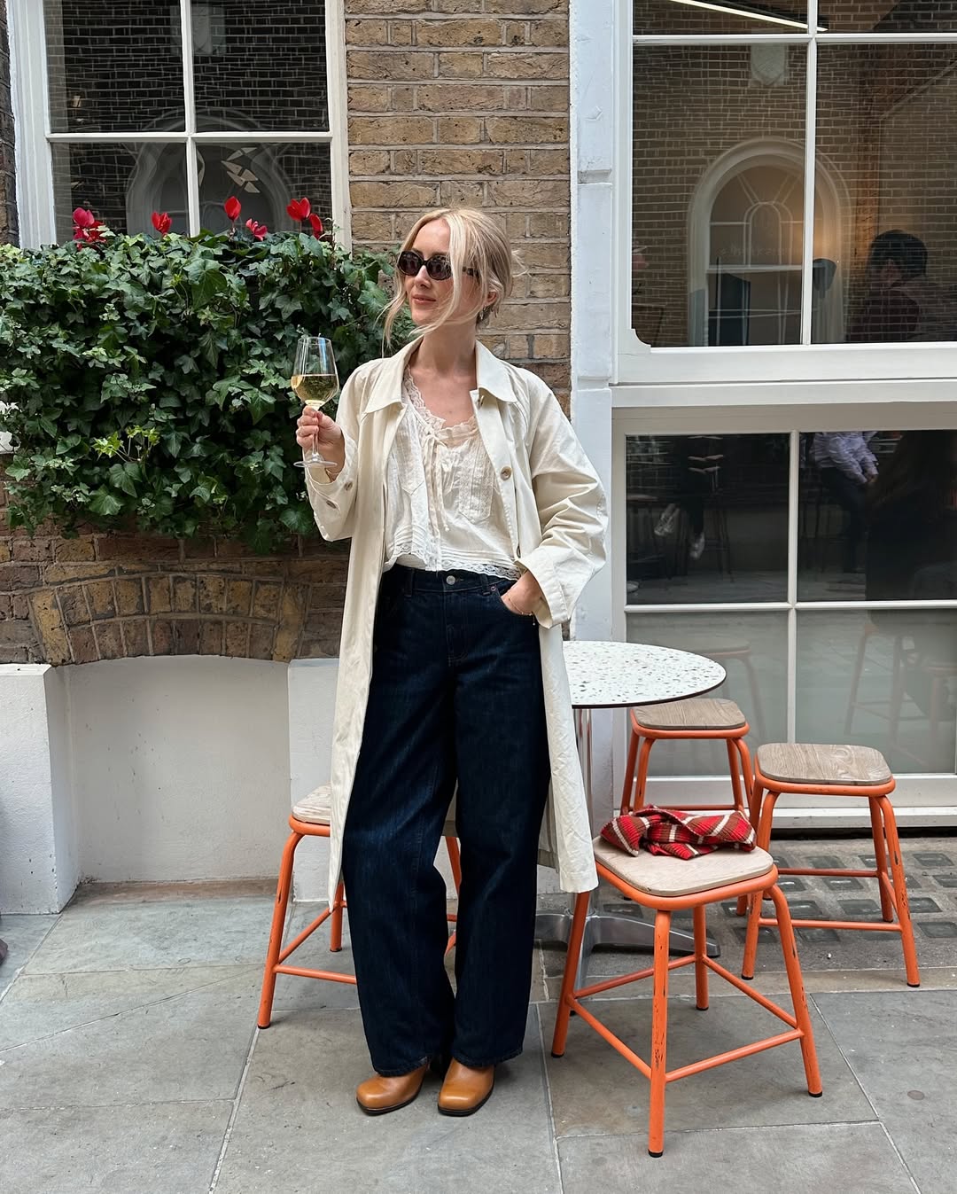 @chloekathbutler wears a white blouse, trench coat, jeans and boots