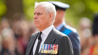 Prince Andrew wearing medals and a gray suit walking outside