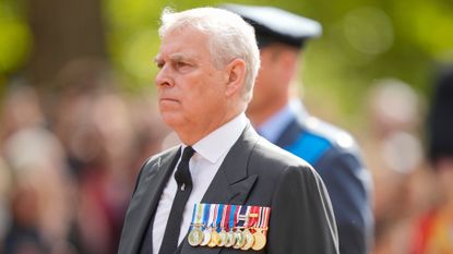 Prince Andrew wearing medals and a gray suit walking outside