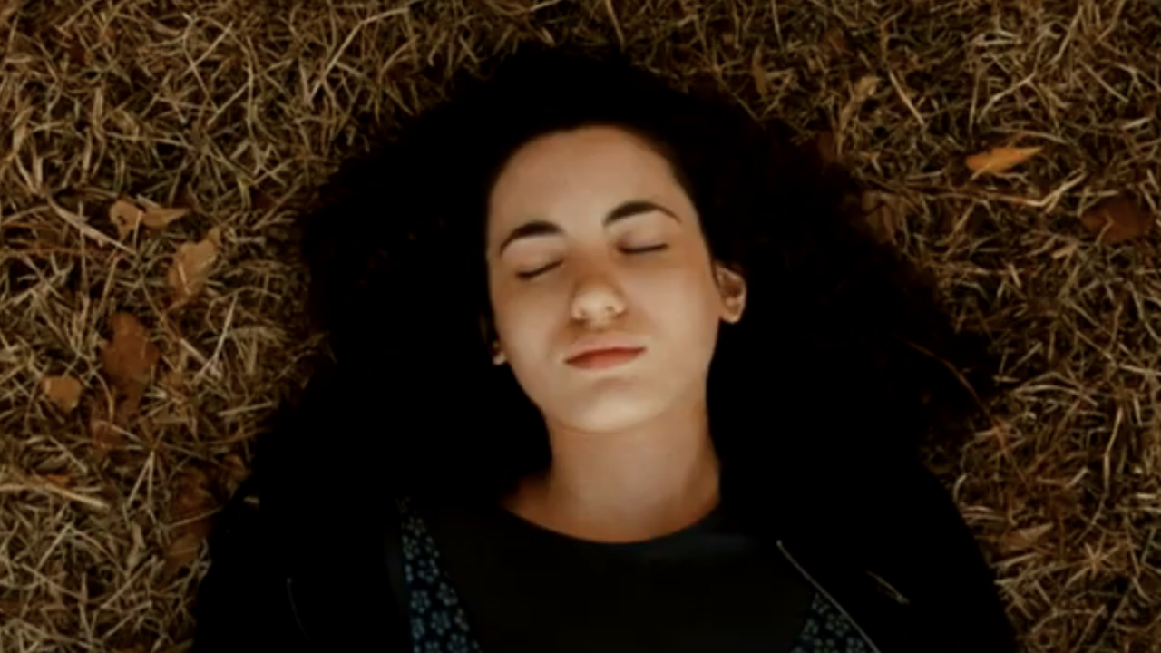 Ivana Baquero as Louisa James laying on the ground, eyes closed in The New Daughter