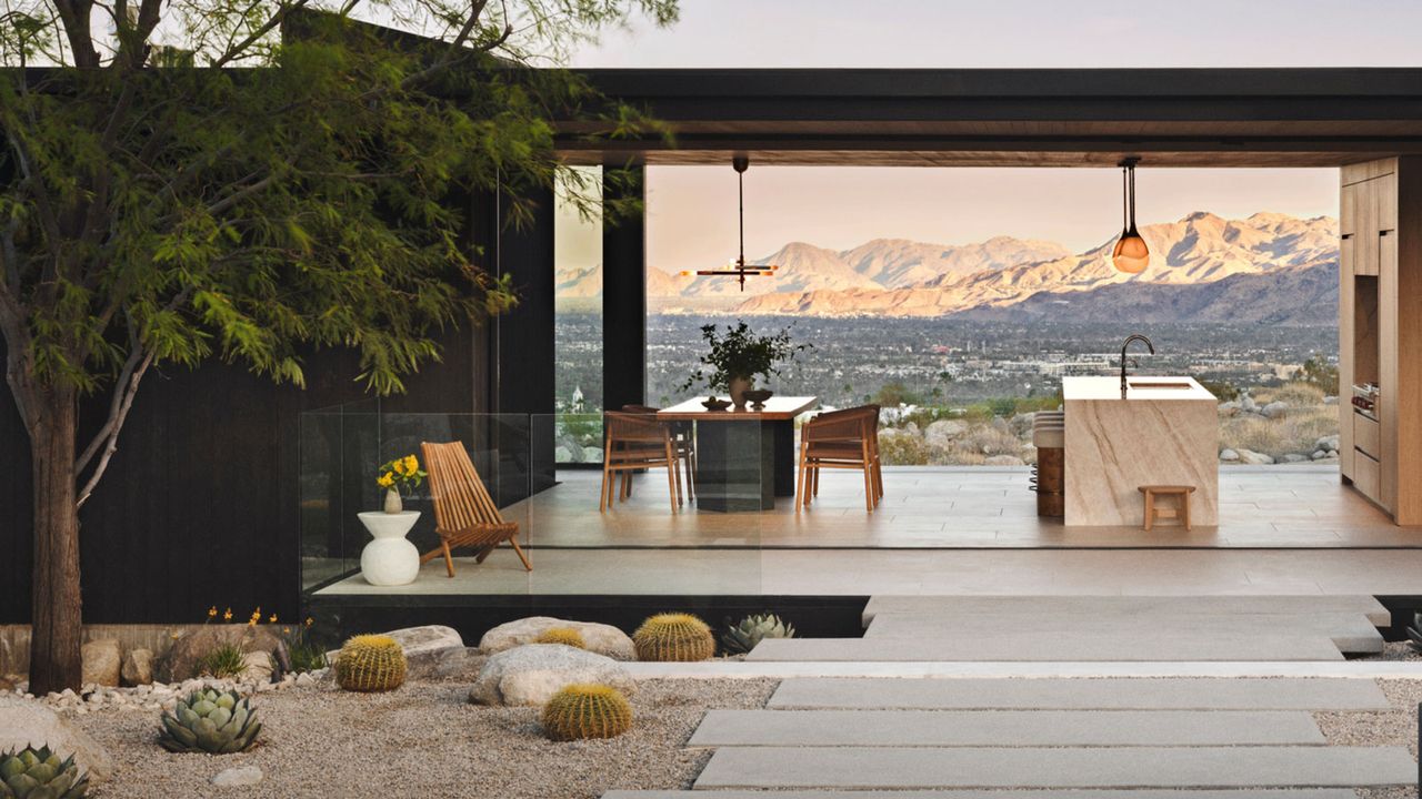 desert modernist landscaping design with rocks, gravel, plants and pavers, with a pergola and outdoor kitchen, and view to mountains beyond