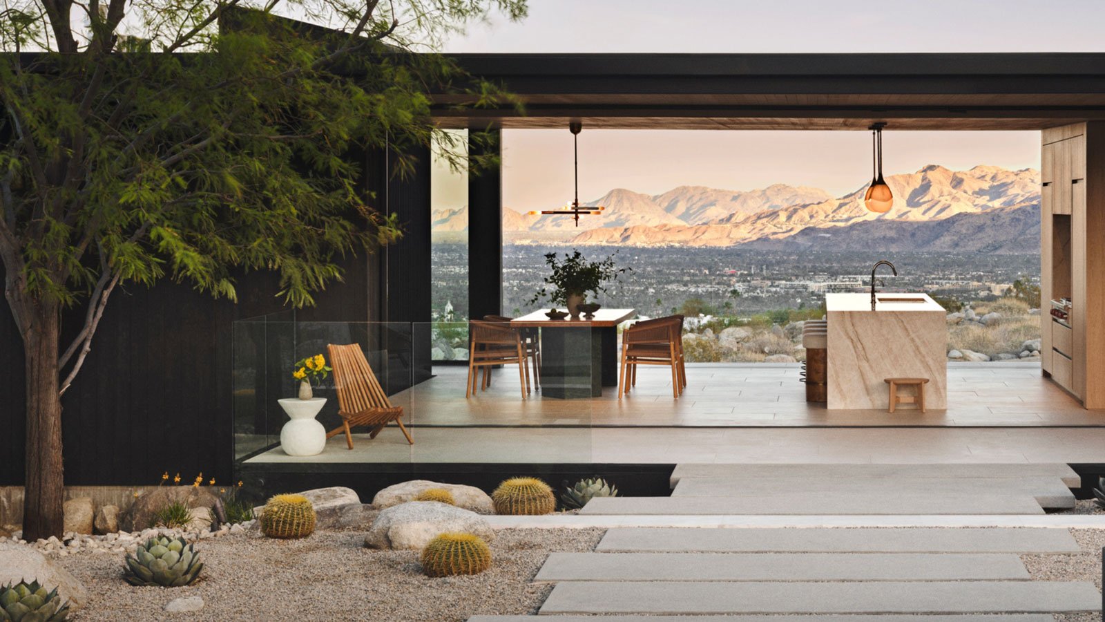 desert modernist landscaping design with rocks, gravel, plants and pavers, with a pergola and outdoor kitchen, and view to mountains beyond