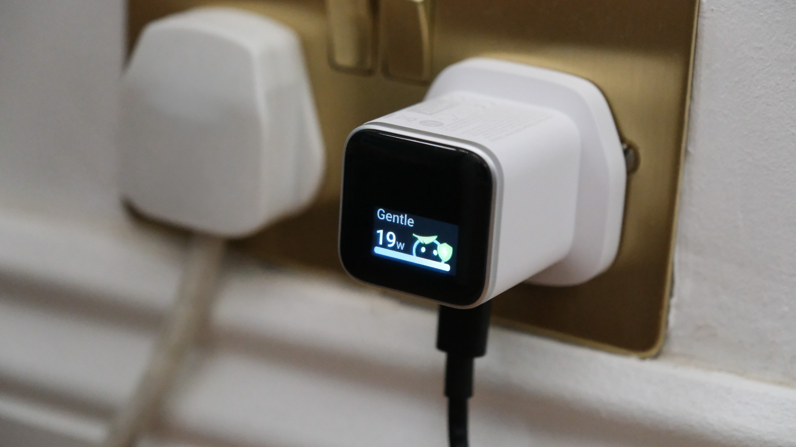 Anker Nano Charger plugged into a wall socket, with its display showing &amp;ldquo;Gentle&amp;rdquo; charging at 19W.