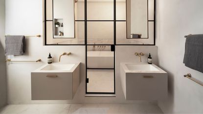 A bathroom with two large squar sinks, a large black framed glass door and a bathtub visible through it