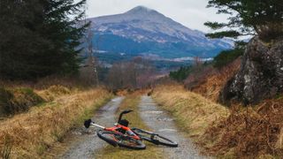 A bike lying on a gravel road with a view of Ban Lomond in the distance