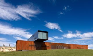 The box embedded in the ground is clad in ribs of rusted Corten steel.