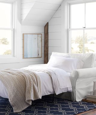 white shiplapped coastal room with a white armchair sleeper sofa made up for a guest with white bedding and a blue rug