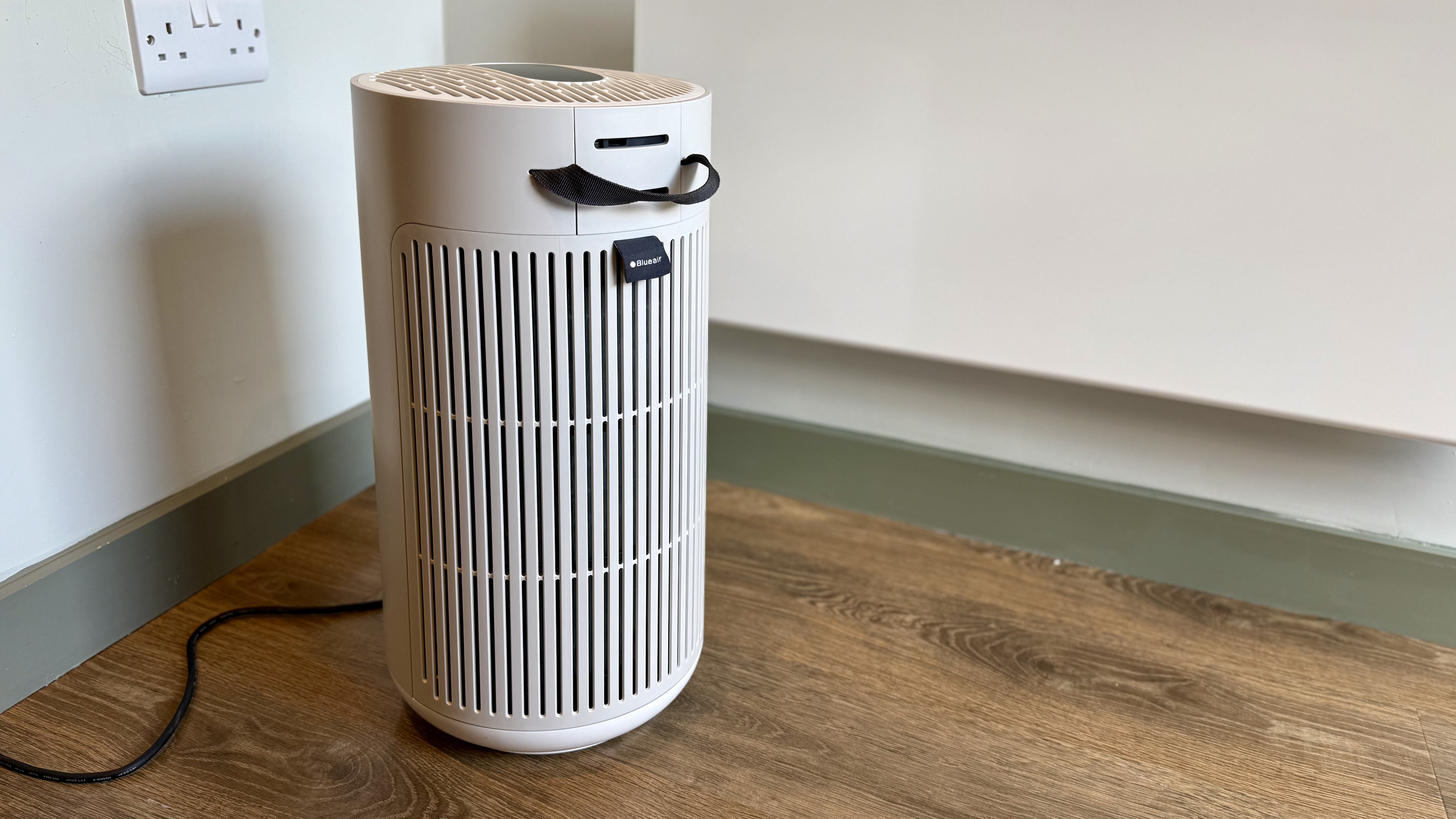 A photo of the Blueair T20i Air Purifier with its remote in a room with white walls and laminated wooden floors