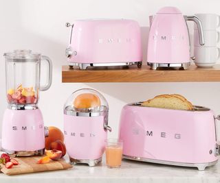 A pink smeg toaster, kettle, juicer, and blender on a countertop