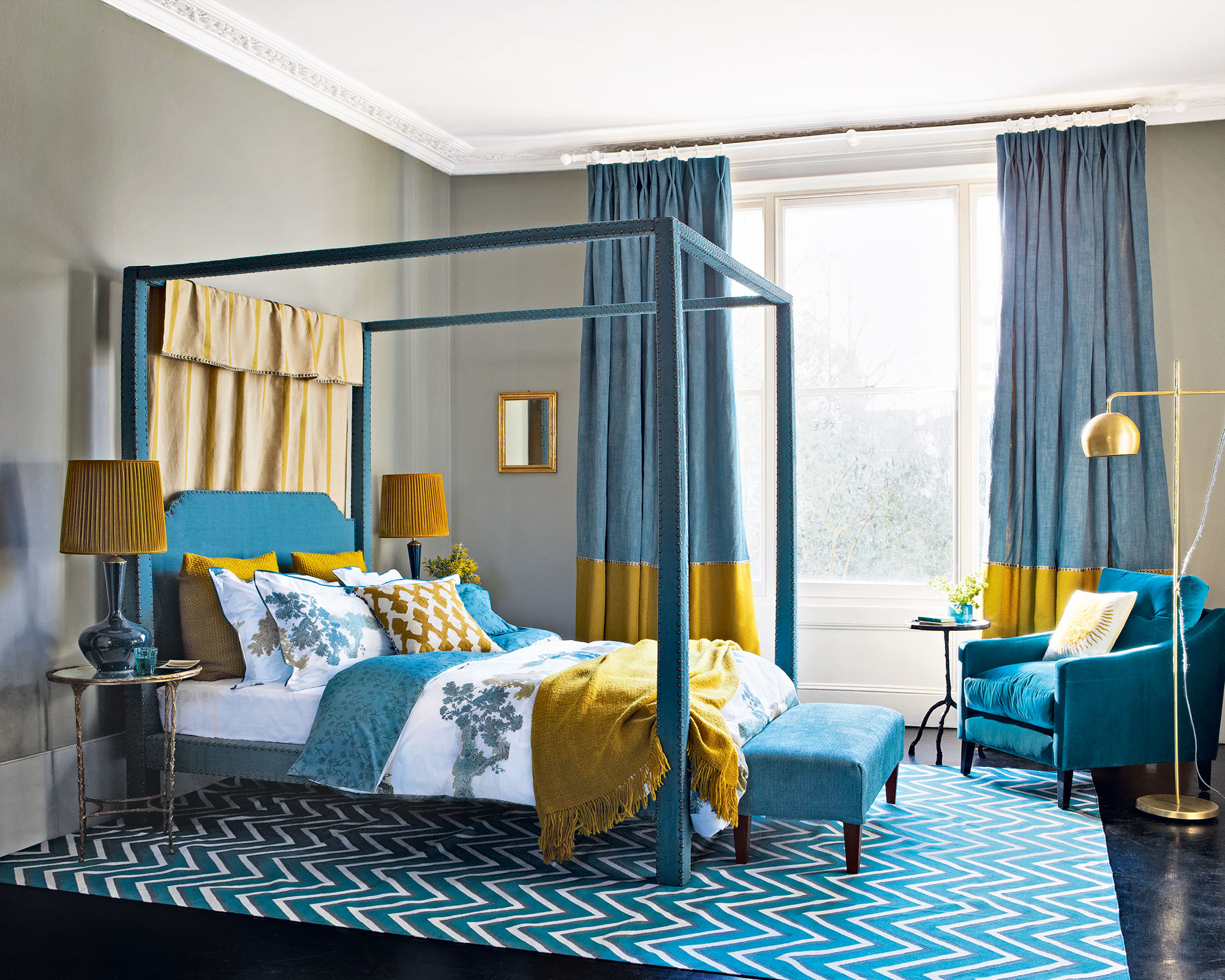 A blue bedroom with a four poster bed, yellow accents and a gold floor lamp