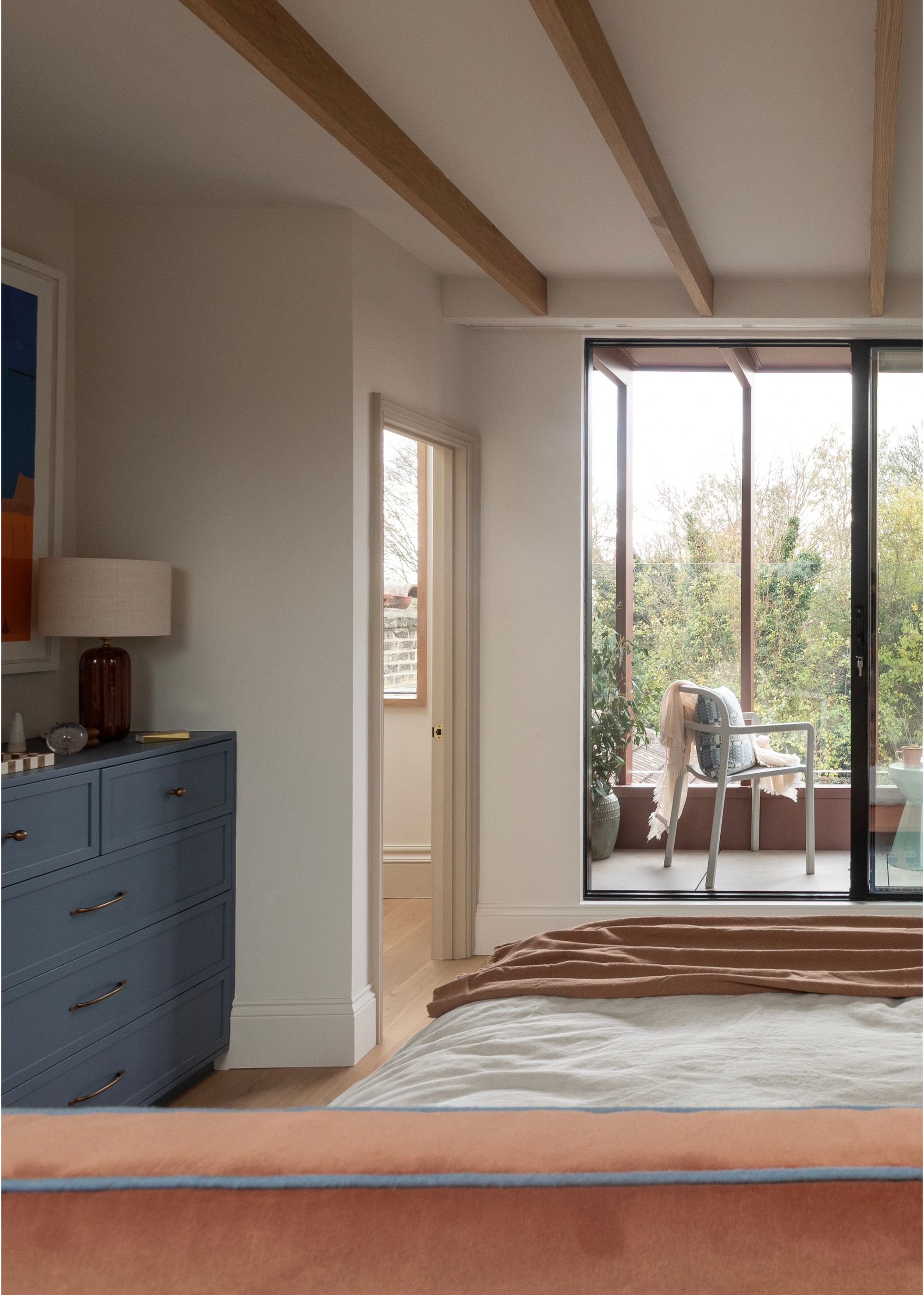 A loft conversion bedroom with wood beam ceilings and a private balcony with sliding black doors