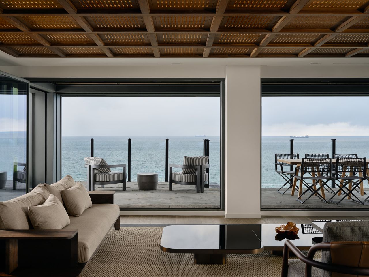 modern living room with lattice coffered ceiling, view out to balcony and lake beyond, beige sofas, black glass coffee table