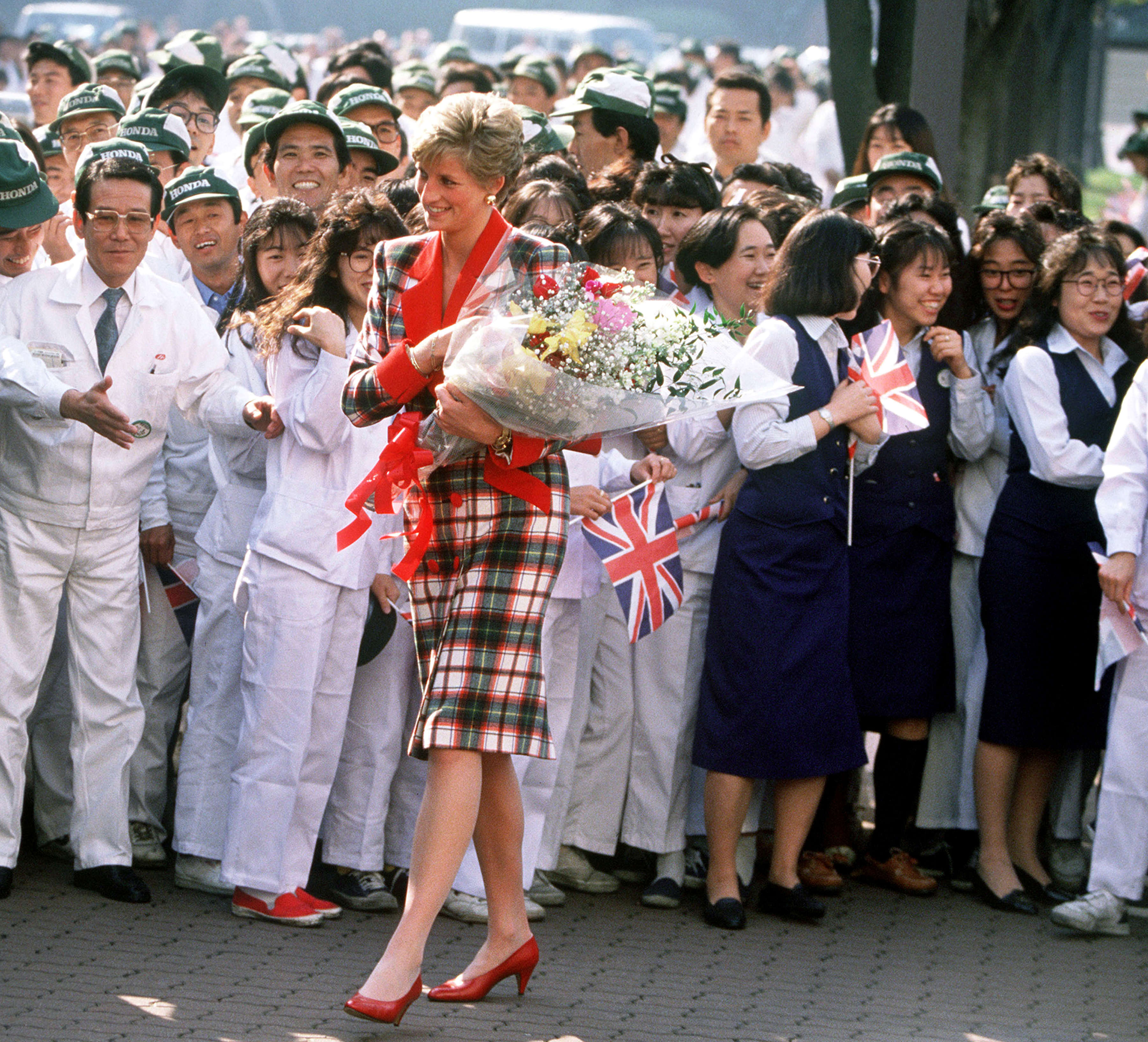 The Princess of Wales with workers at the Honda factory in Tokyo, during a visit to Japan, November 1990. She is wearing a Catherine Walker tartan coat dress