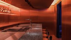 A dramatically lit bar features warm red light spreading across its chrome and stone surfaces.