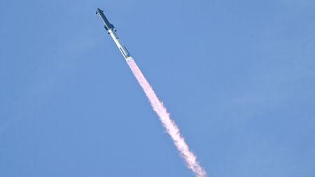 a rocket launches against a light blue sky. 