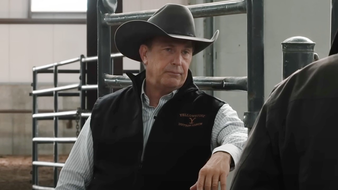 Kevin Costner as John Dutton leaning against a gate on Yellowstone.