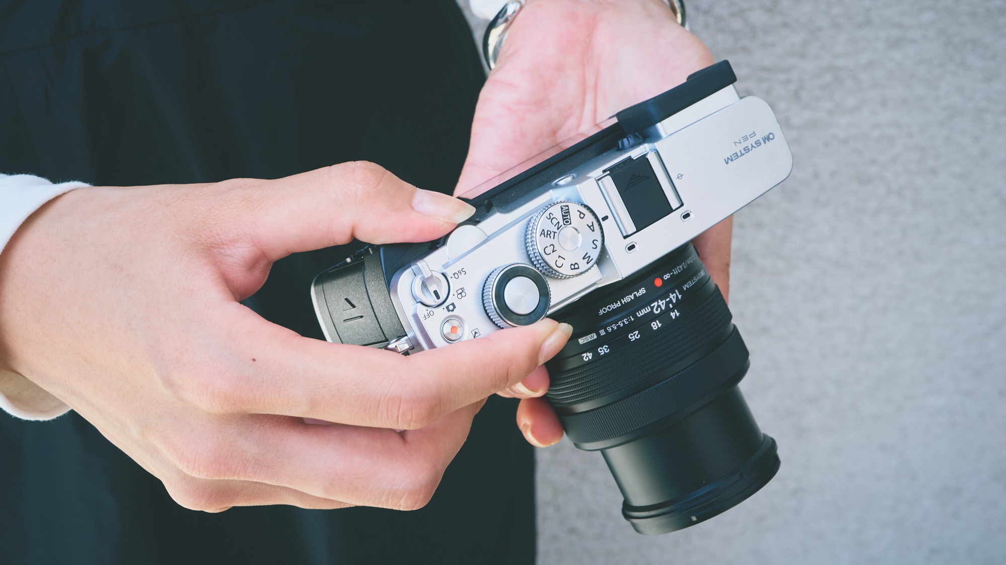 OM System PEN camera in person's hands and they are tilting the camera down to see the screen