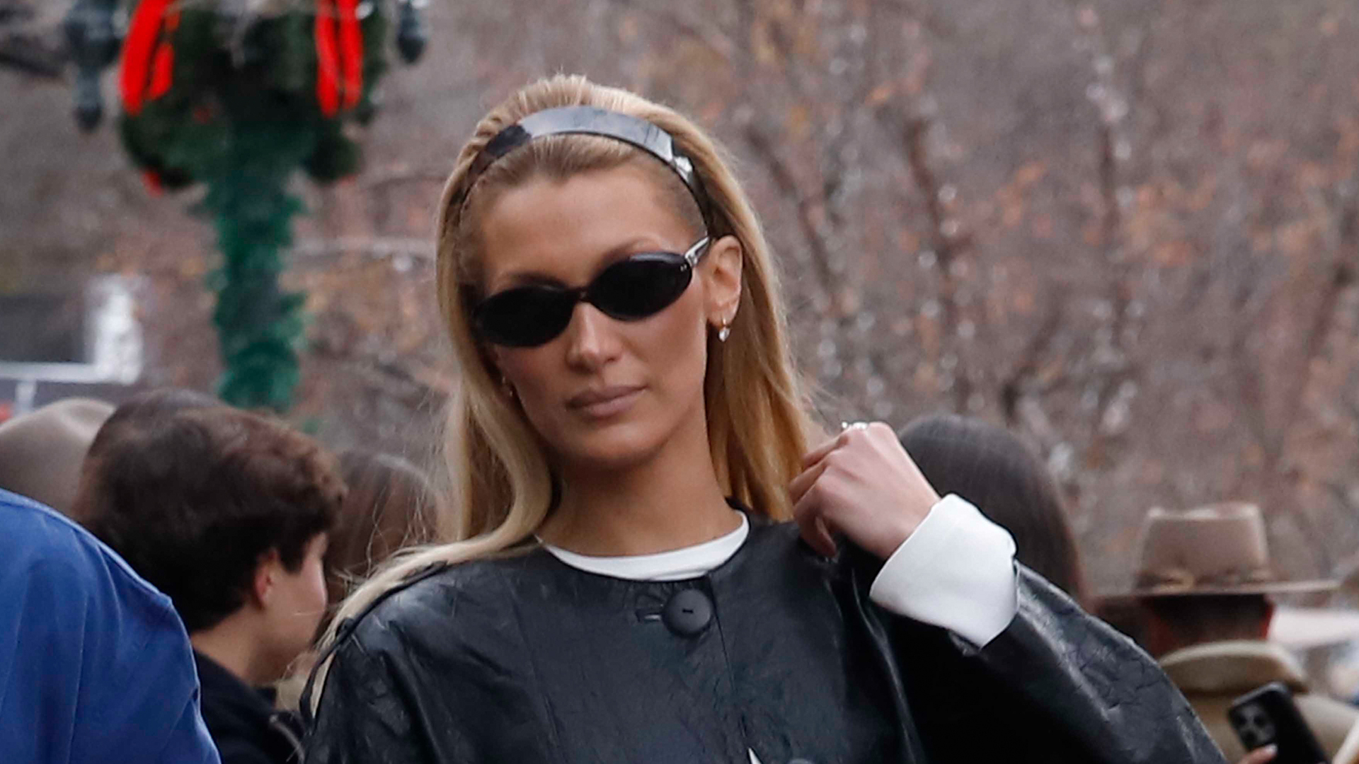 Bella Hadid wearing a black leather jacket, white long-sleeve top, and white jeans.