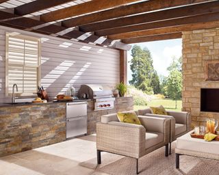 An example of south facing garden ideas showing an outdoor kitchen and living space with sofas and a built in BBQ